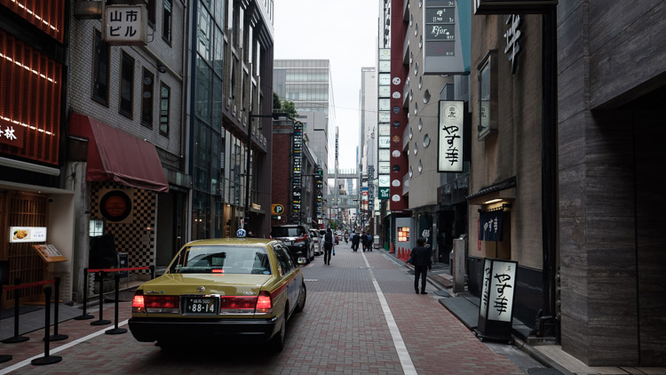 A classic yellow Tokyo taxi parked on a narrow Ginza side street lined with vertical signs and lanterns