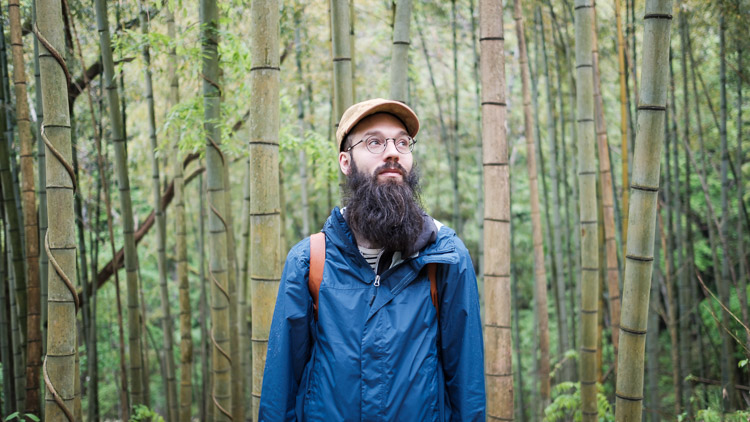 David looks upward while standing among the tall green stalks of a bamboo grove