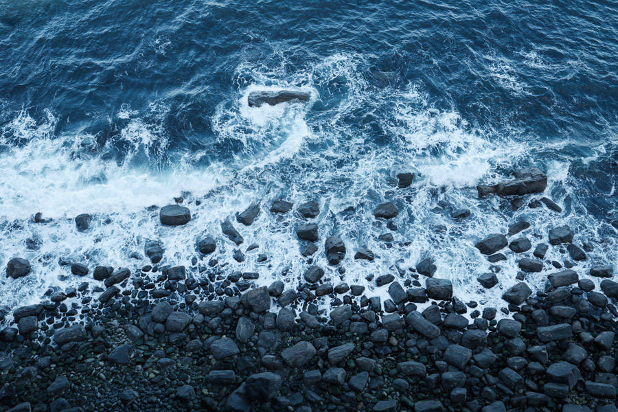 Looking straight down at white surf washing over dark boulders on a rocky Scottish shore