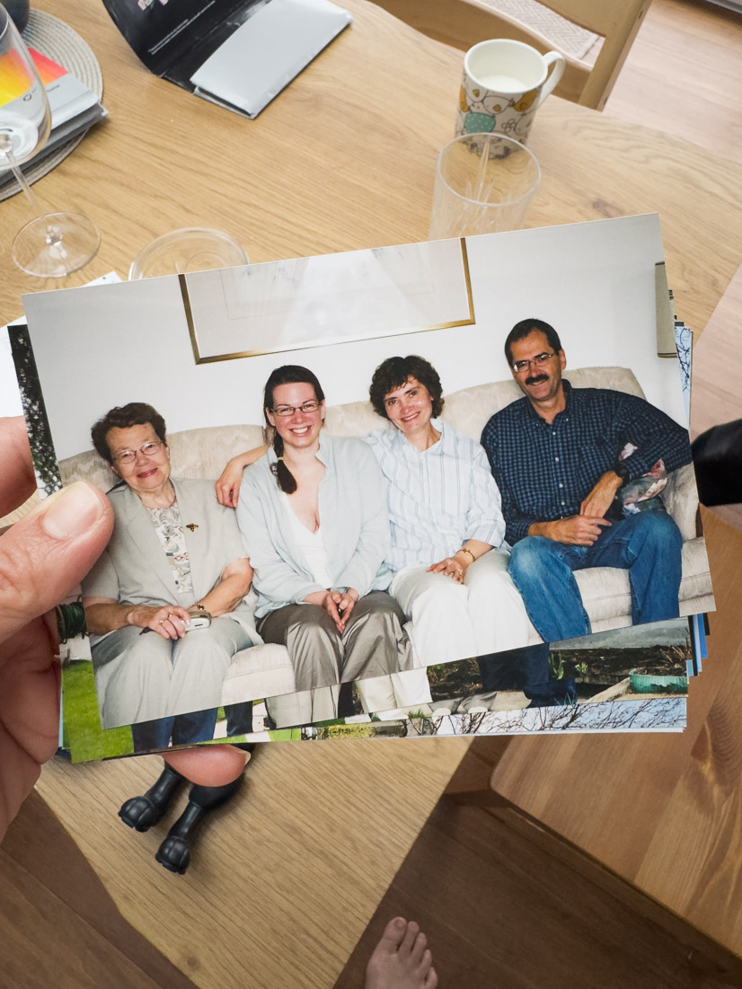 A hand holds an old family print of four relatives smiling together on a couch